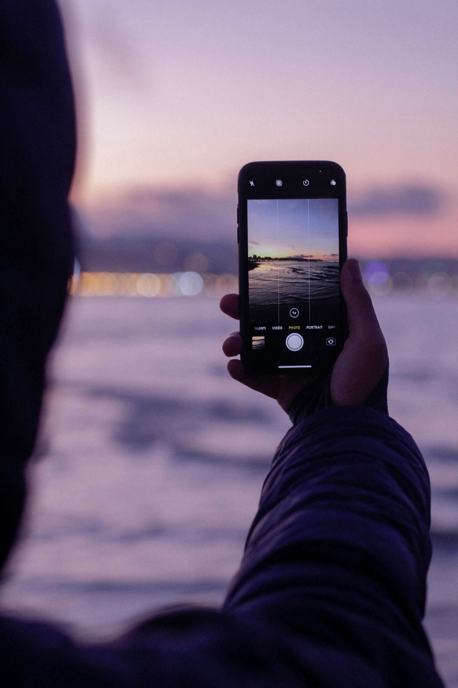 Mensch fotografiert einen Sonnenuntergang am Meer mit dem Smartphone